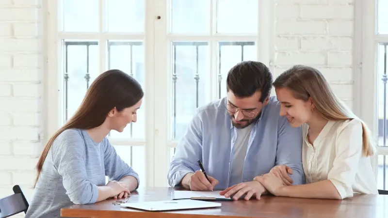 A landlord and tenants sit at a table signing a rental agreement