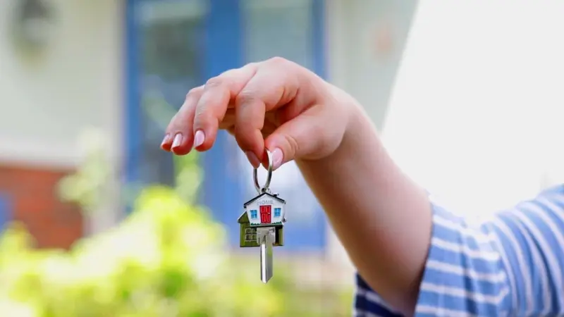 A Tenant in Indiana holds a house-shaped keychain while standing outside a rental home