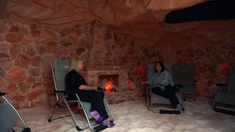 Two guests relax in lounge chairs inside a softly lit salt cave in Carmel