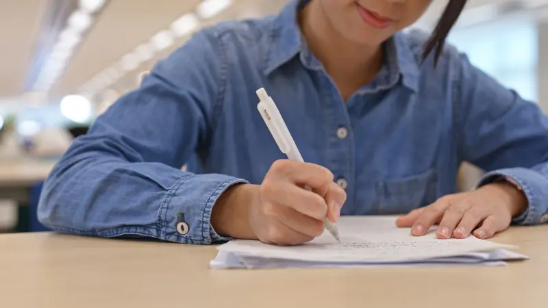 A student writes an essay at a desk during early application preparation