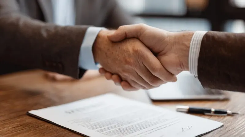 Two people shaking hands over a document on a desk