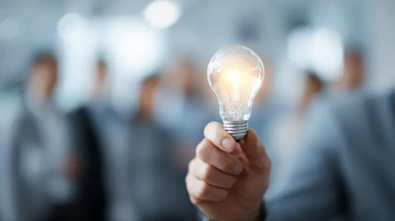 Person holding a glowing light bulb with a blurred business team in the background